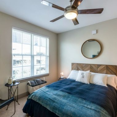 bedroom with large window and ceiling fan with bed and blue accent decor
